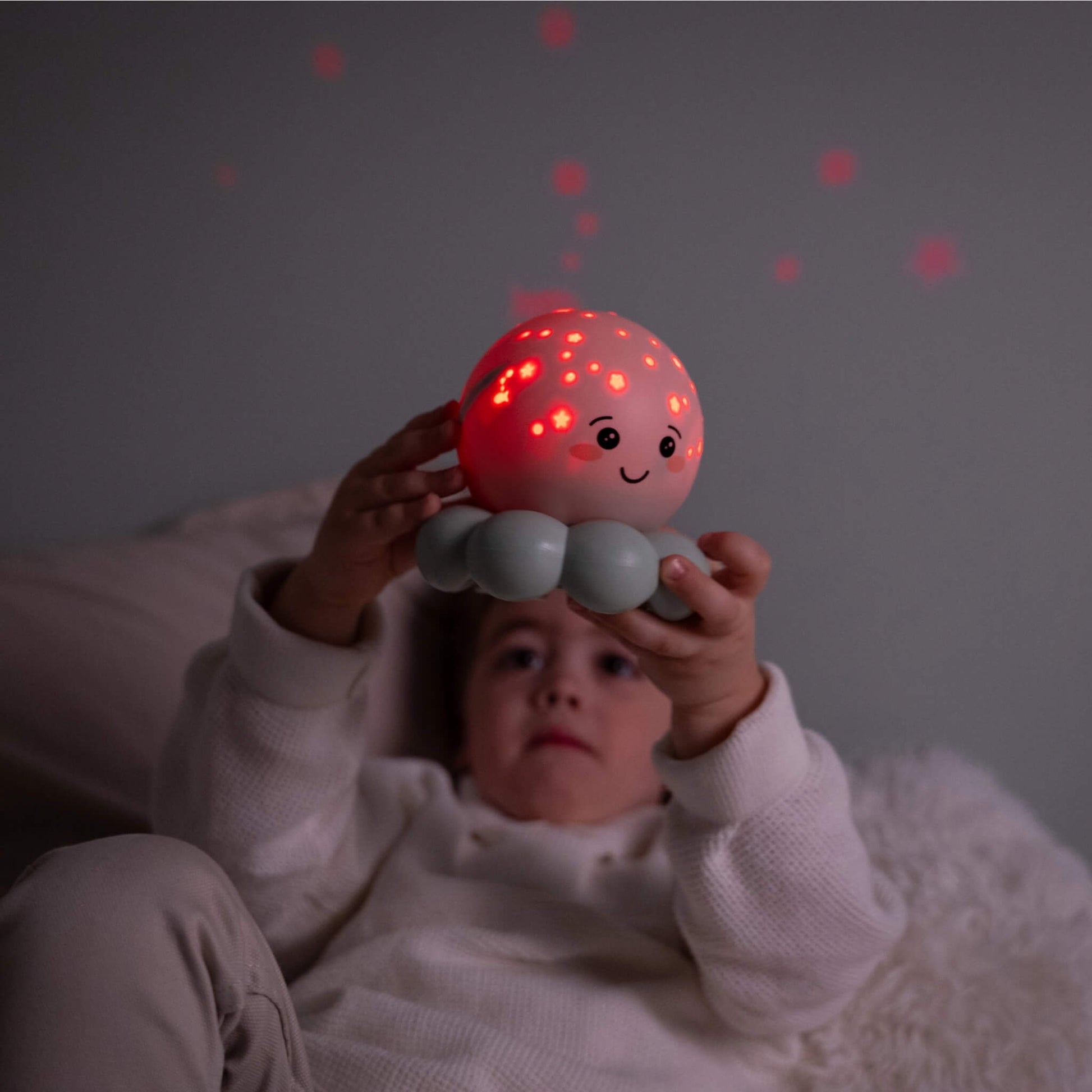 A child lying in bed holding a glowing red octopus night light.