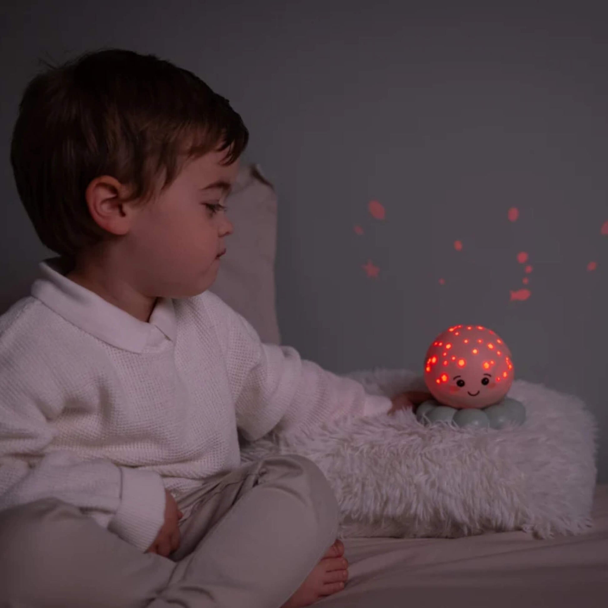 A child watching a glowing octopus night light projecting red shapes onto the bedroom wall.