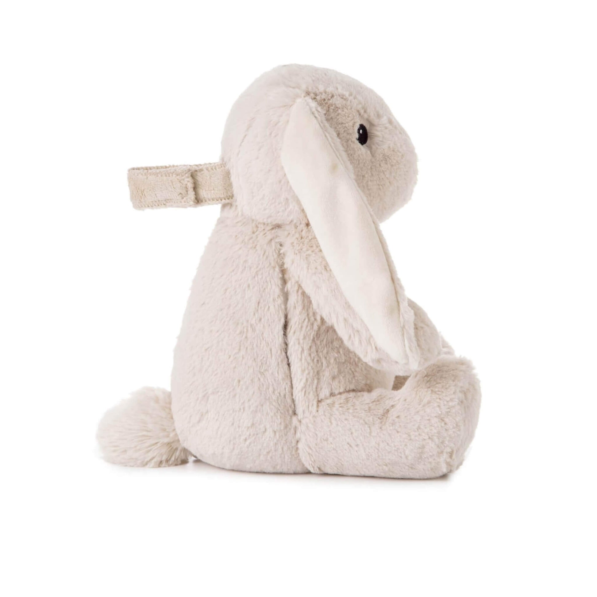 Side profile of a soft bunny toy with floppy ears, short tail and a fabric strap attached to its back.