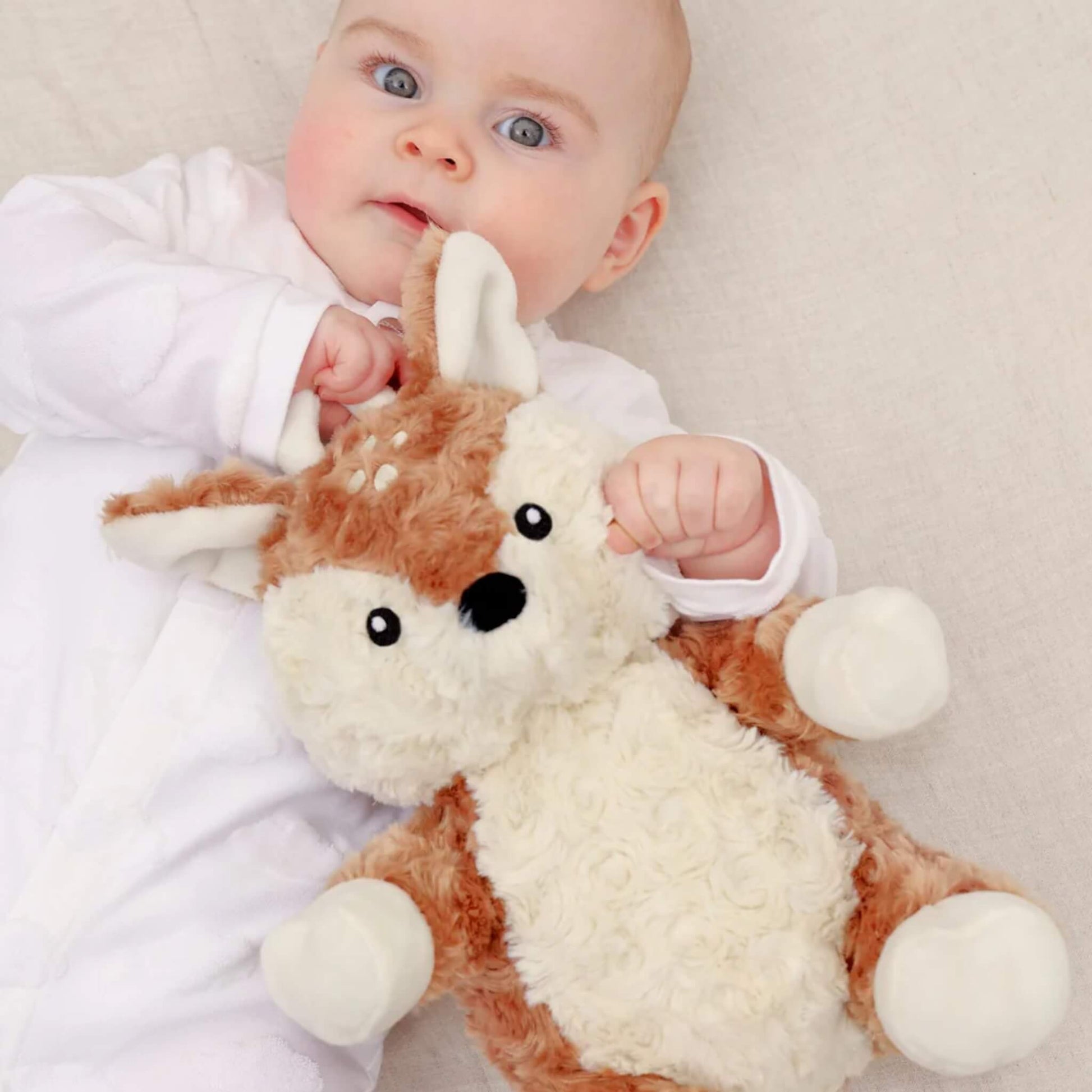 Baby lying on their back holding a soft fawn plush toy with antlers and floppy ears.