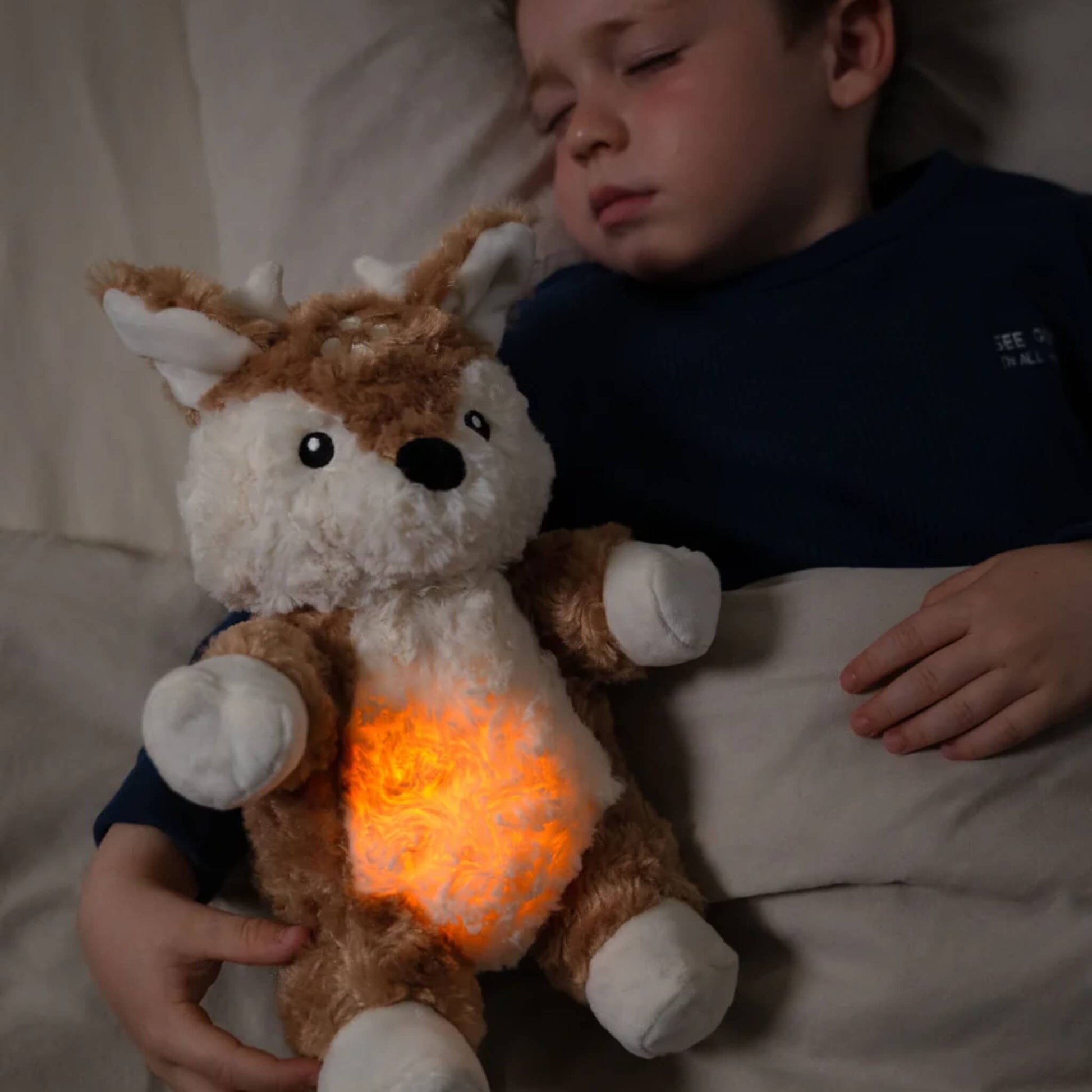 Child asleep in bed holding a fawn plush toy with an orange glowing tummy against their chest.
