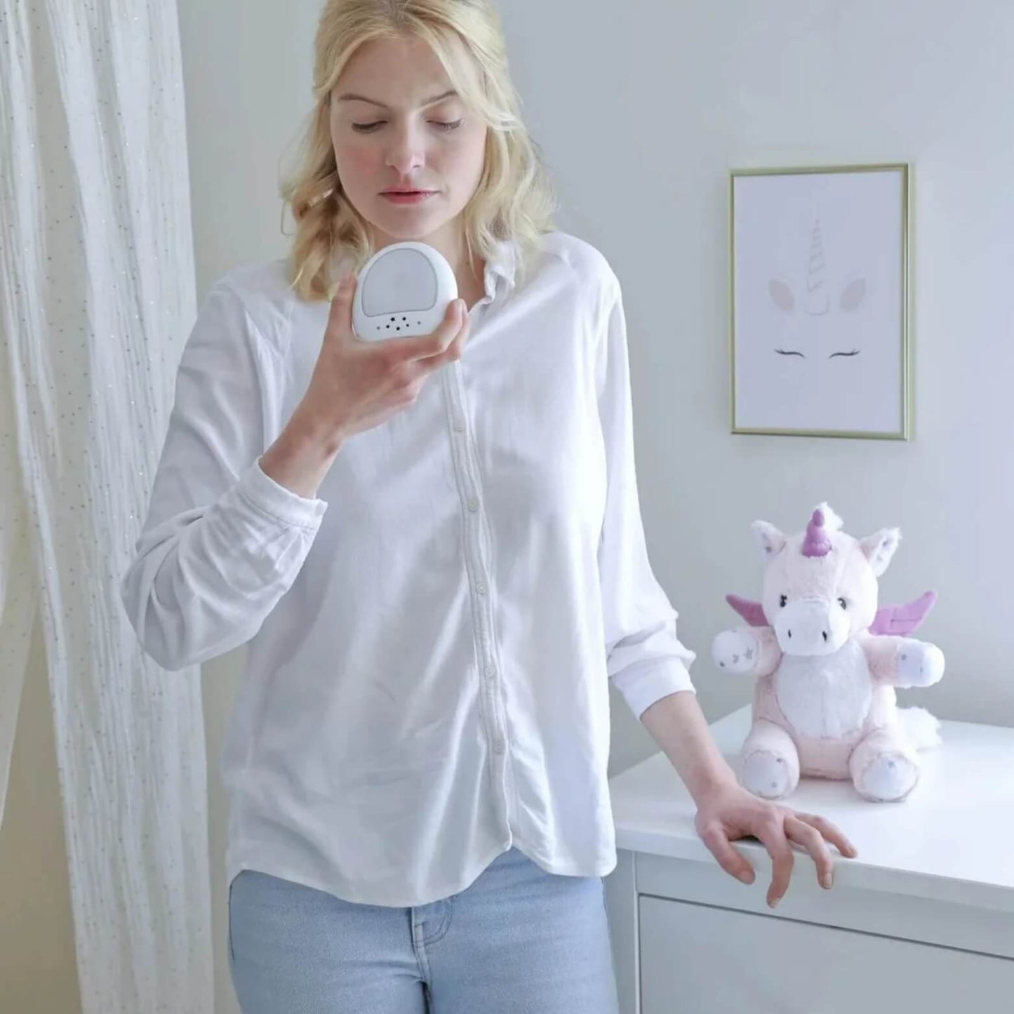 Woman speaking into the removable night-light unit while the unicorn plush toy sits on a dresser in the background.