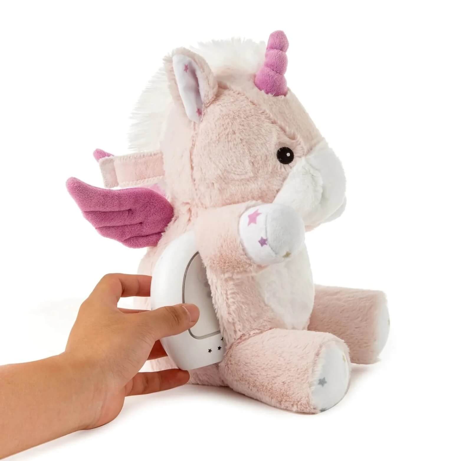 Hand removing the glowing night-light unit from the back pocket of the unicorn plush toy.