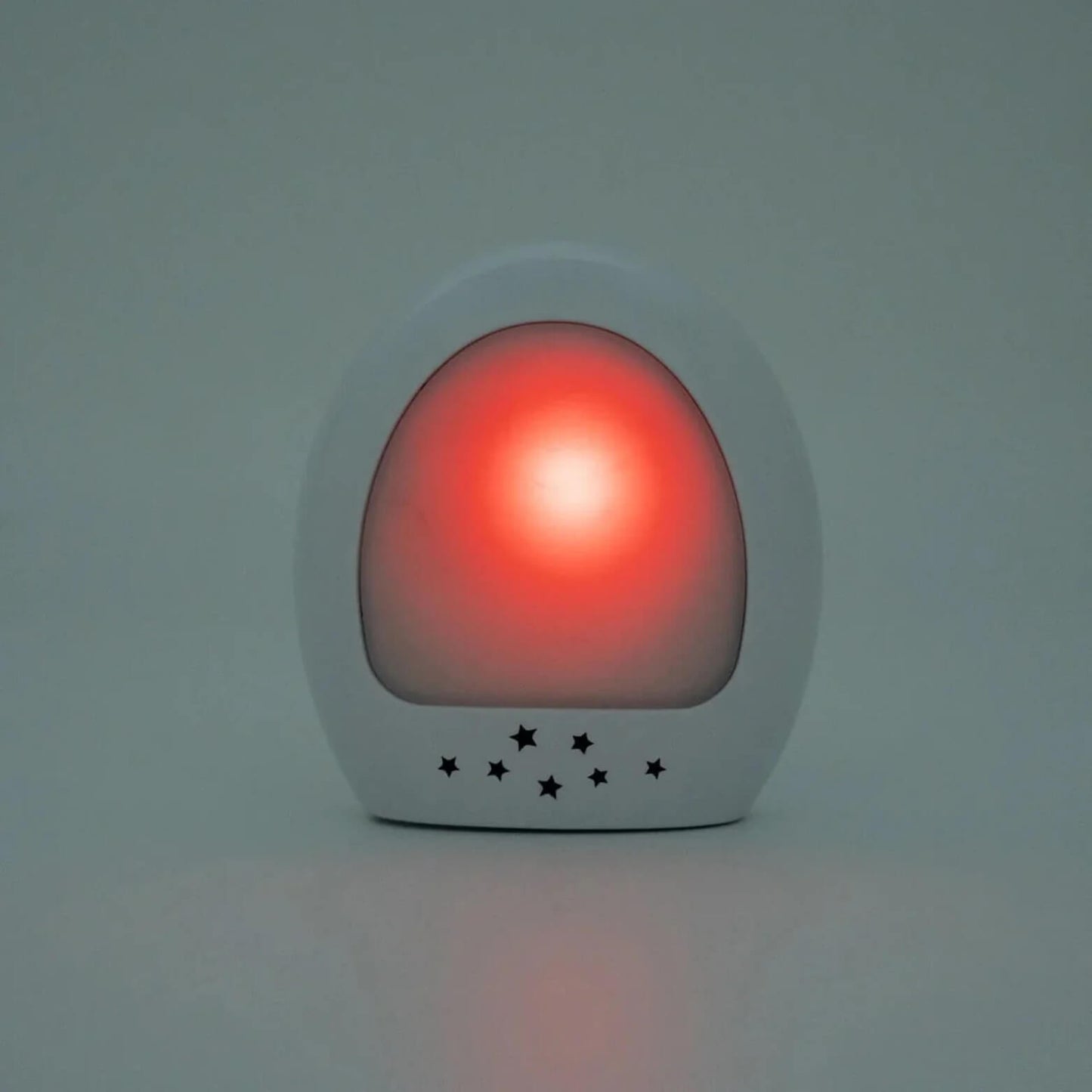 Close-up of the glowing white night-light unit, lit red with small star-shaped cutouts along the base.
