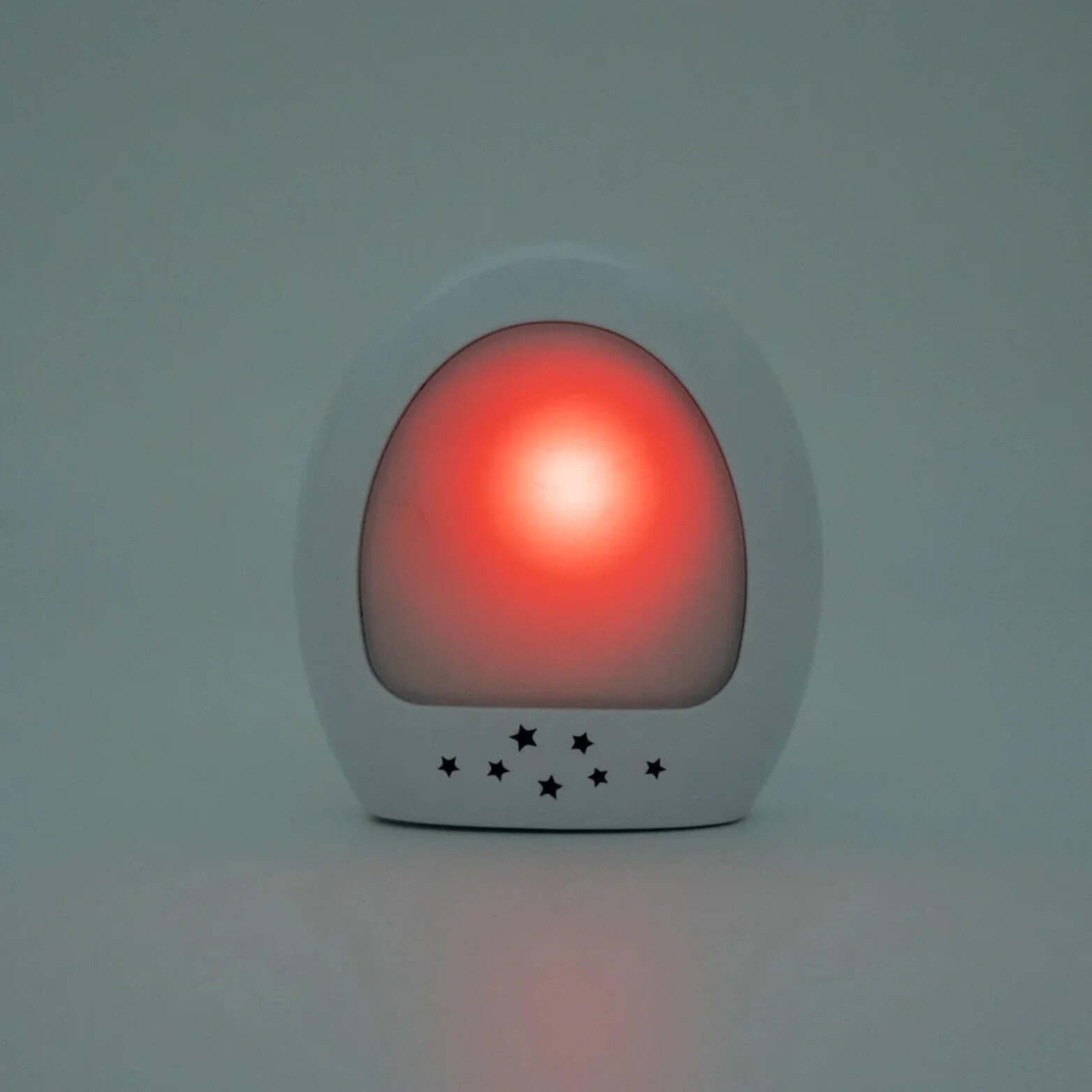 Close-up of the glowing white night-light unit, lit red with small star-shaped cutouts along the base.