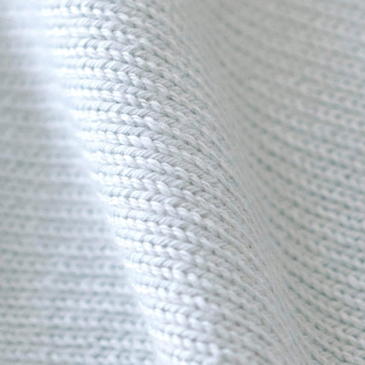 Close-up of pale blue organic cotton knit showing the soft texture and neatly finished knitted edge of the baby comforter.