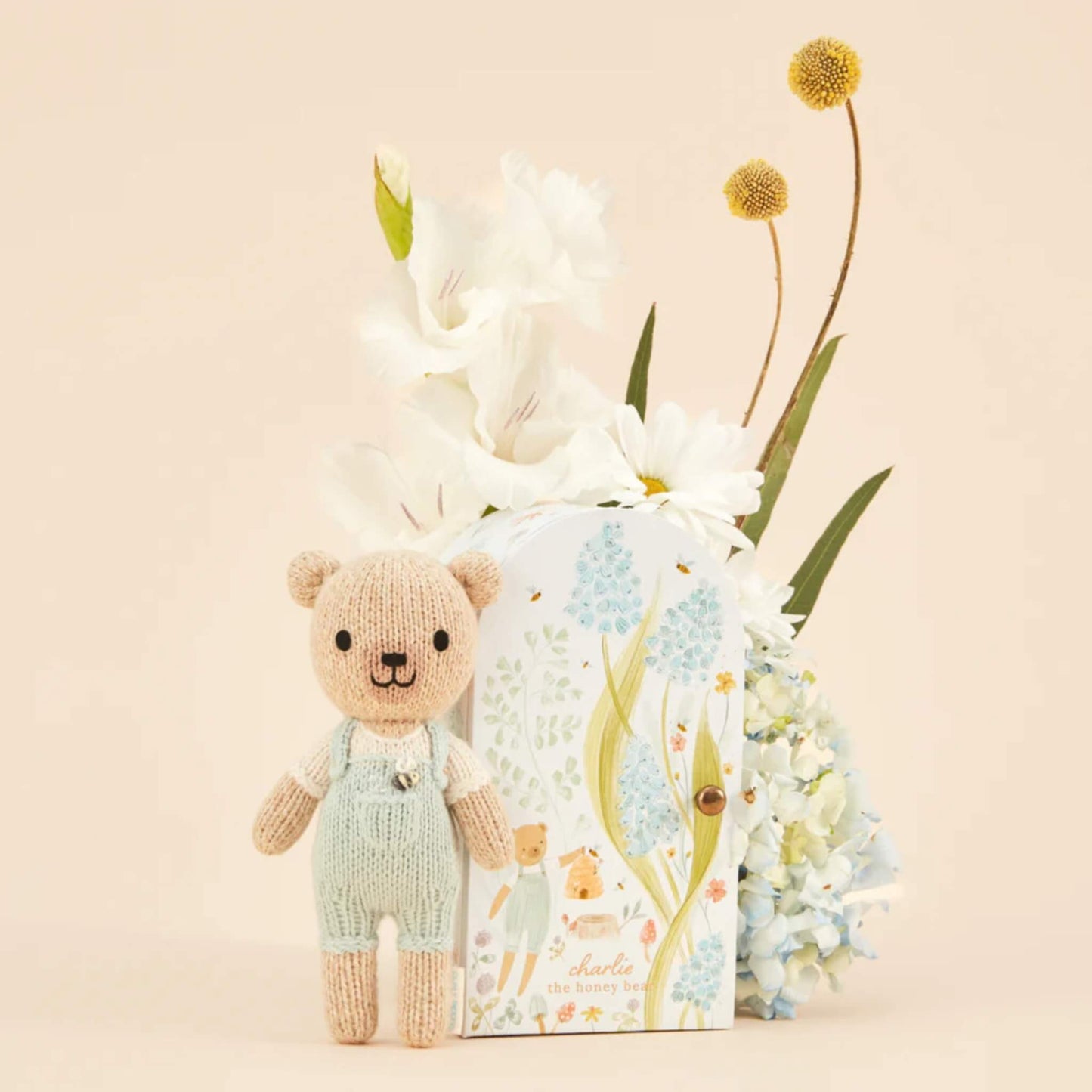 A small knitted doll standing beside a decorative keepsake box with hand-painted floral illustrations and soft pastel tones.