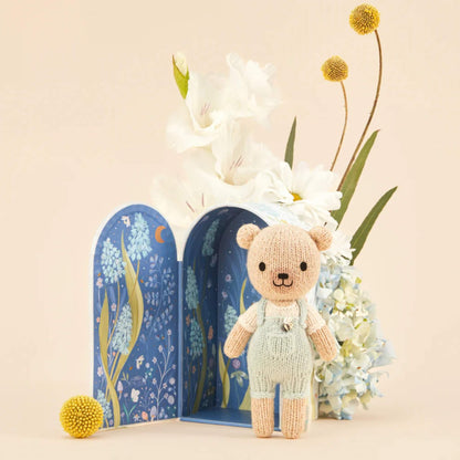 An illustrated Tiny home box opened to reveal a dark blue night scene with floral details and a small knitted doll placed in front.