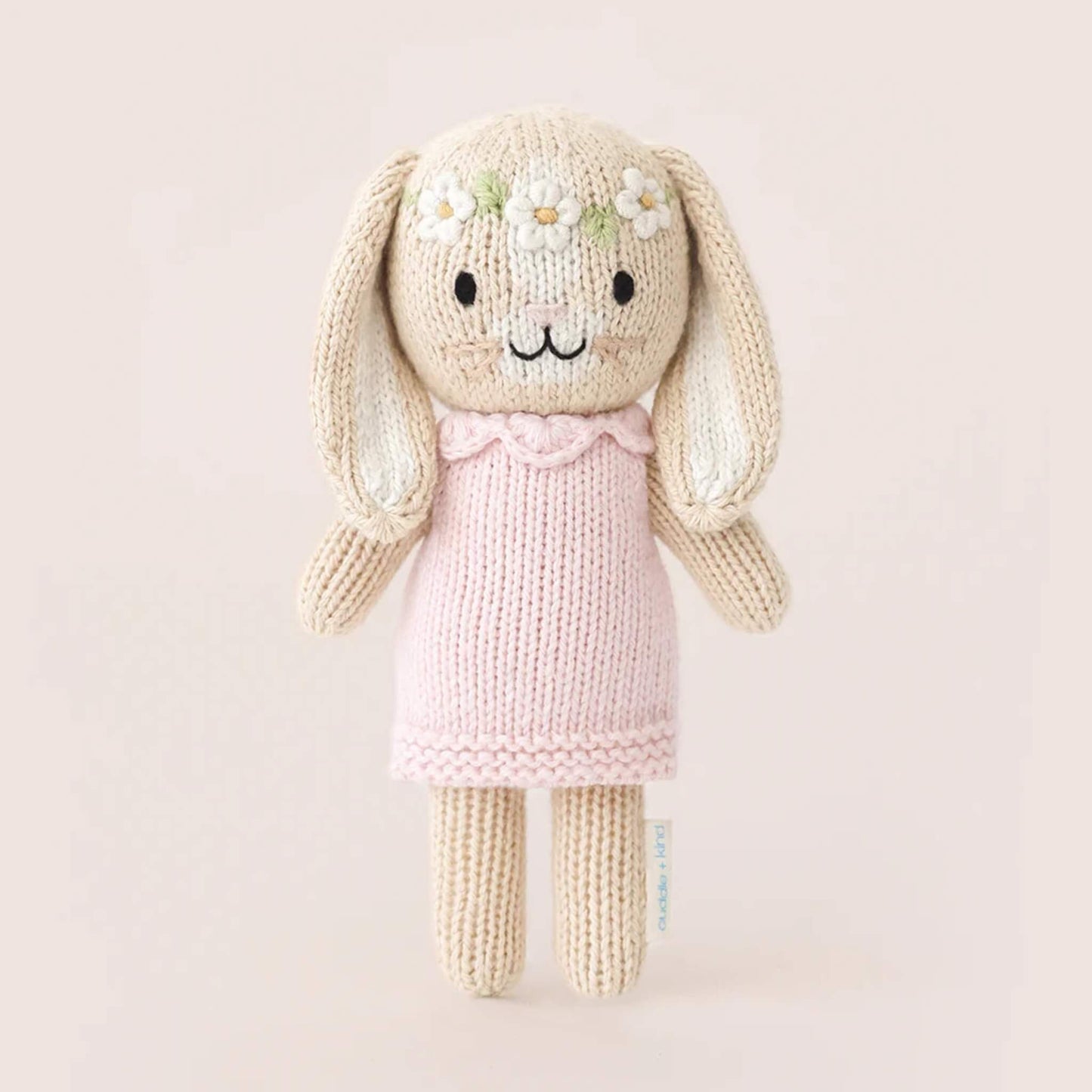 Full view of small knitted bunny soft toy standing upright, wearing a pale pink dress with textured knit finish.