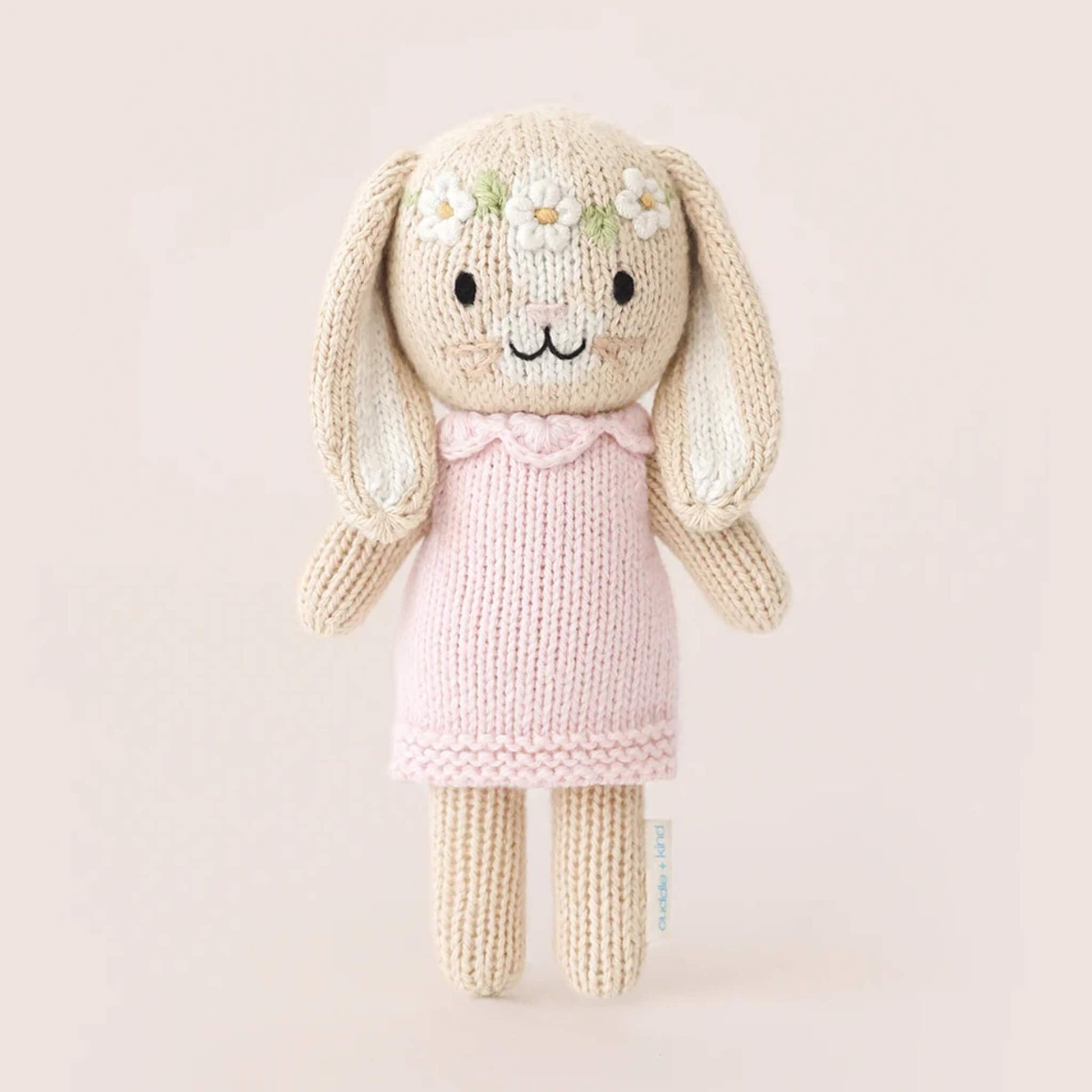 Full view of small knitted bunny soft toy standing upright, wearing a pale pink dress with textured knit finish.