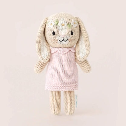 Full view of small knitted bunny soft toy standing upright, wearing a pale pink dress with textured knit finish.