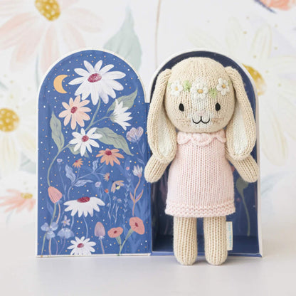 Knitted bunny doll displayed inside open gift box with illustrated night sky and floral interior design.