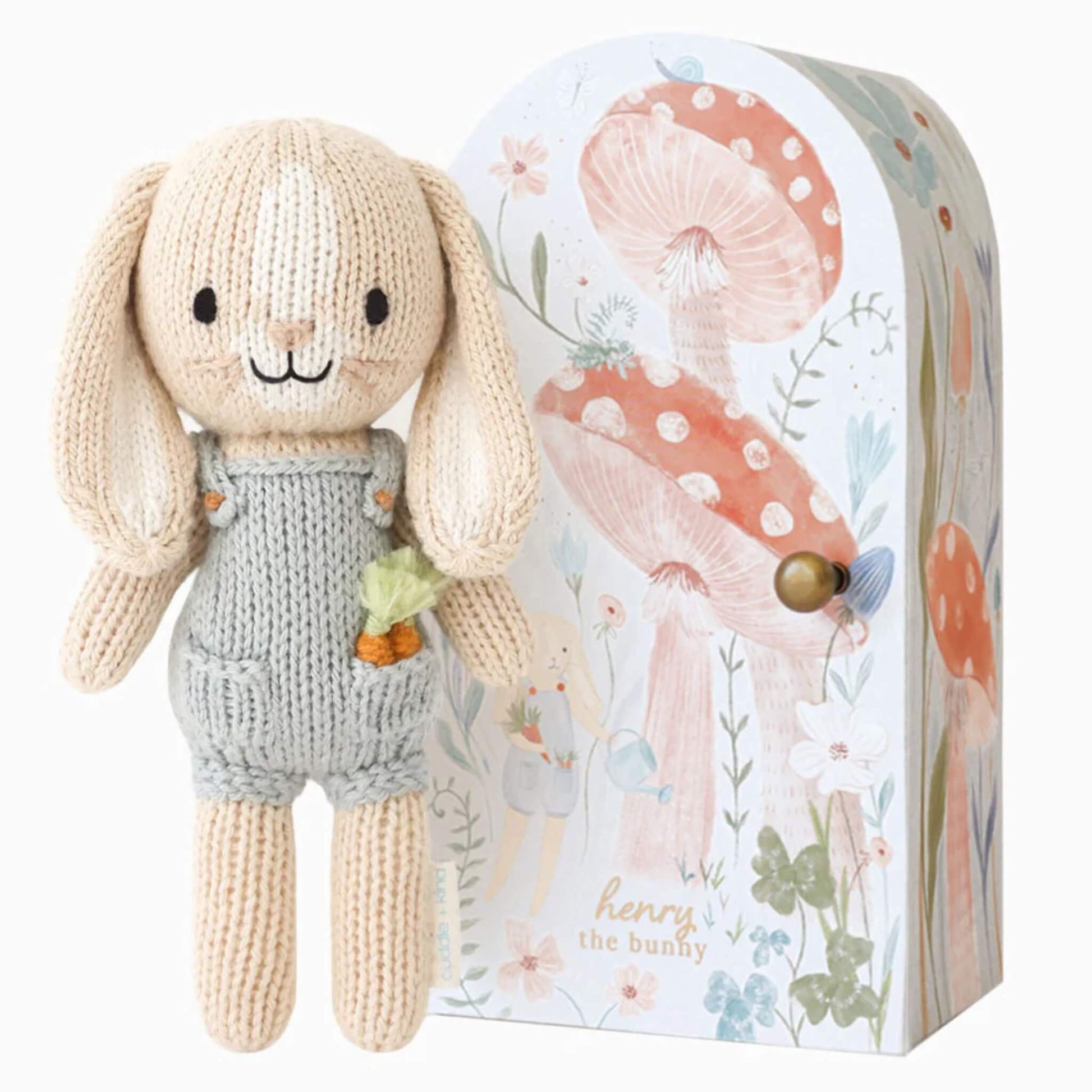 Cuddle + Kind Tiny Collection Henry the Bunny knitted soft toy in grey overalls holding a small carrot, displayed beside illustrated keepsake box.