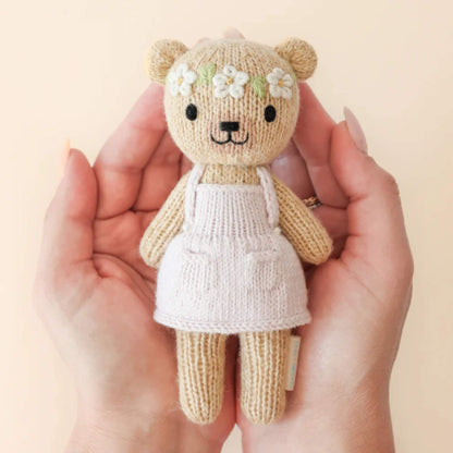 A small hand-knit cotton doll held in two hands, showing scale, soft texture and pale pink outfit with stitched pockets.