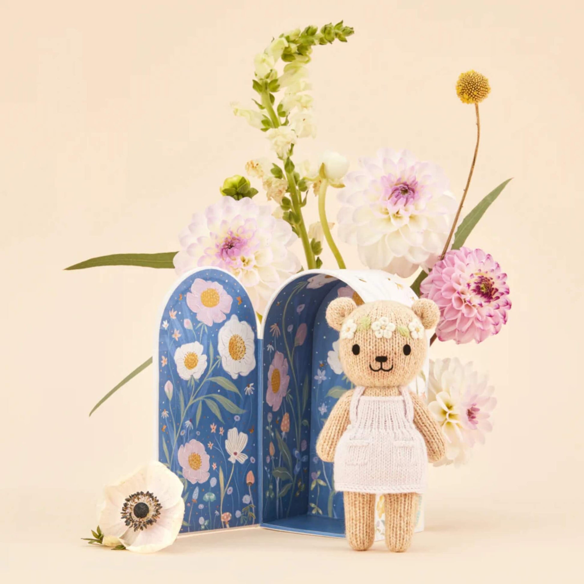 An illustrated Tiny home box opened to reveal a deep blue night scene with floral details and a knitted doll placed in front.