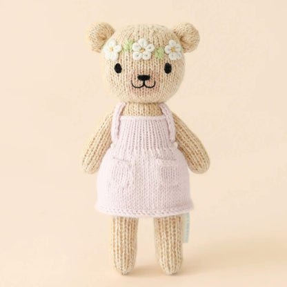 A hand-knit cotton doll standing upright against a neutral background, wearing a pale pink dress with delicate stitched detailing.