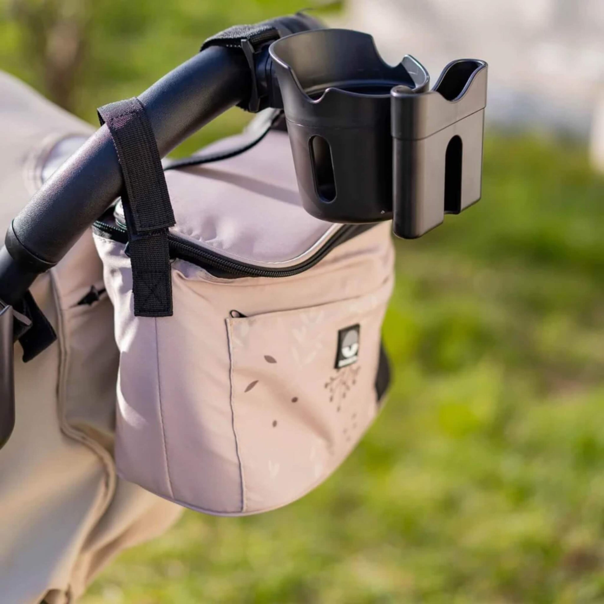Black stroller cup and phone holder attached to a pushchair handlebar alongside a beige stroller organiser bag.