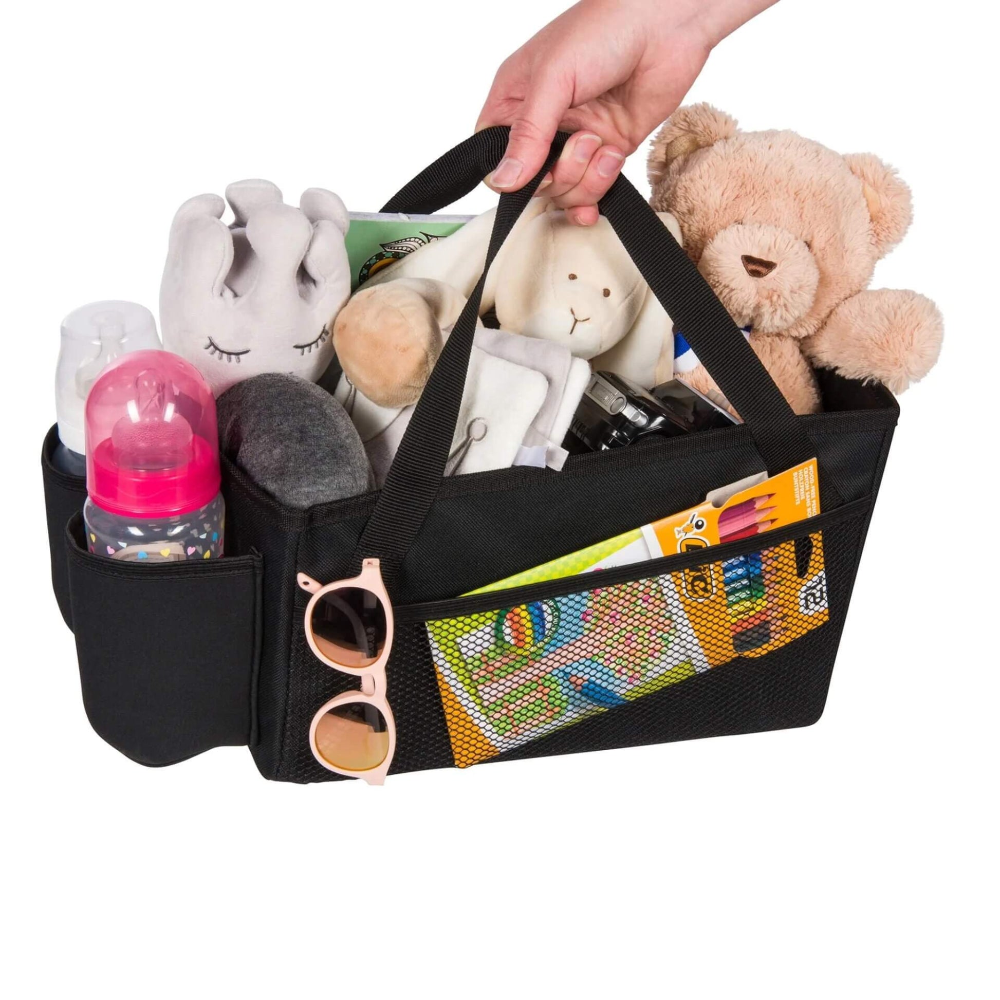 A black car seat basket filled with baby essentials including soft toys, bottles, and colouring supplies, held by one handle.