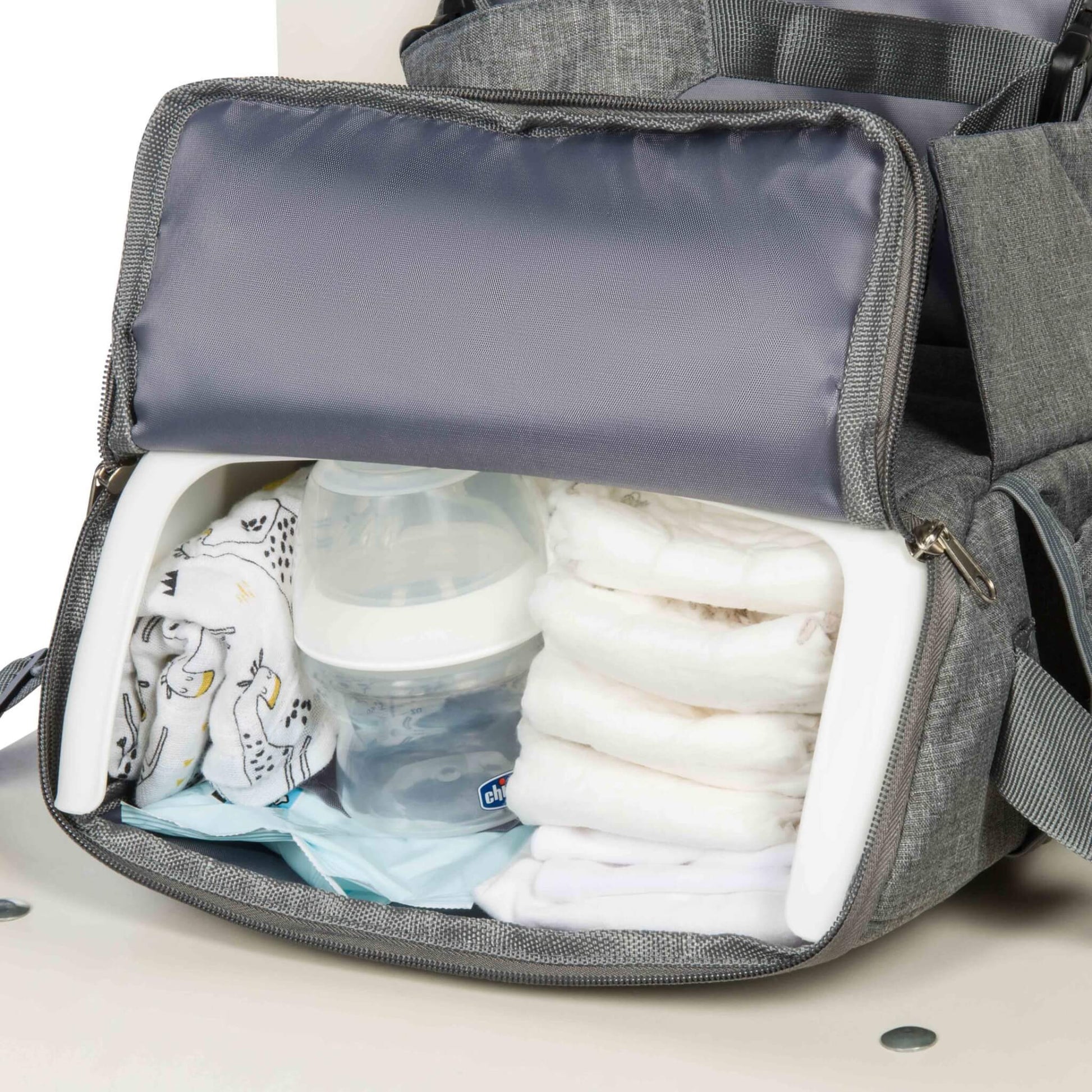 A close-up of an open storage compartment filled with nappies, a baby bottle, wipes, and muslins.