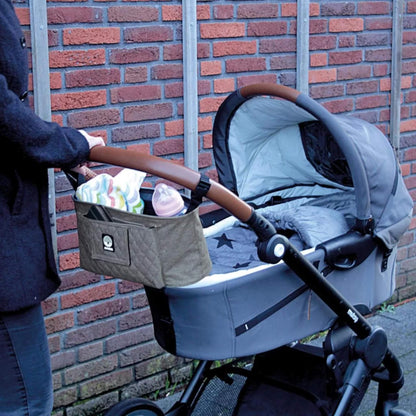 A grey buggy organiser attached to a pushchair handlebar, holding a baby bottle, blanket, and other essentials.