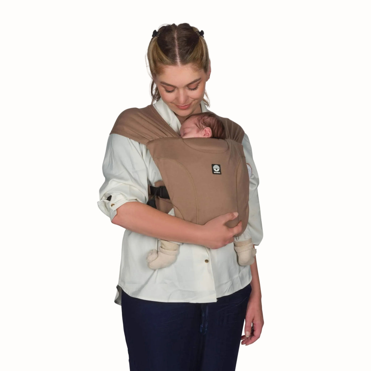 Woman carrying a newborn upright against her chest in a mocha baby carrier with wide fabric shoulder straps and supportive front panel.