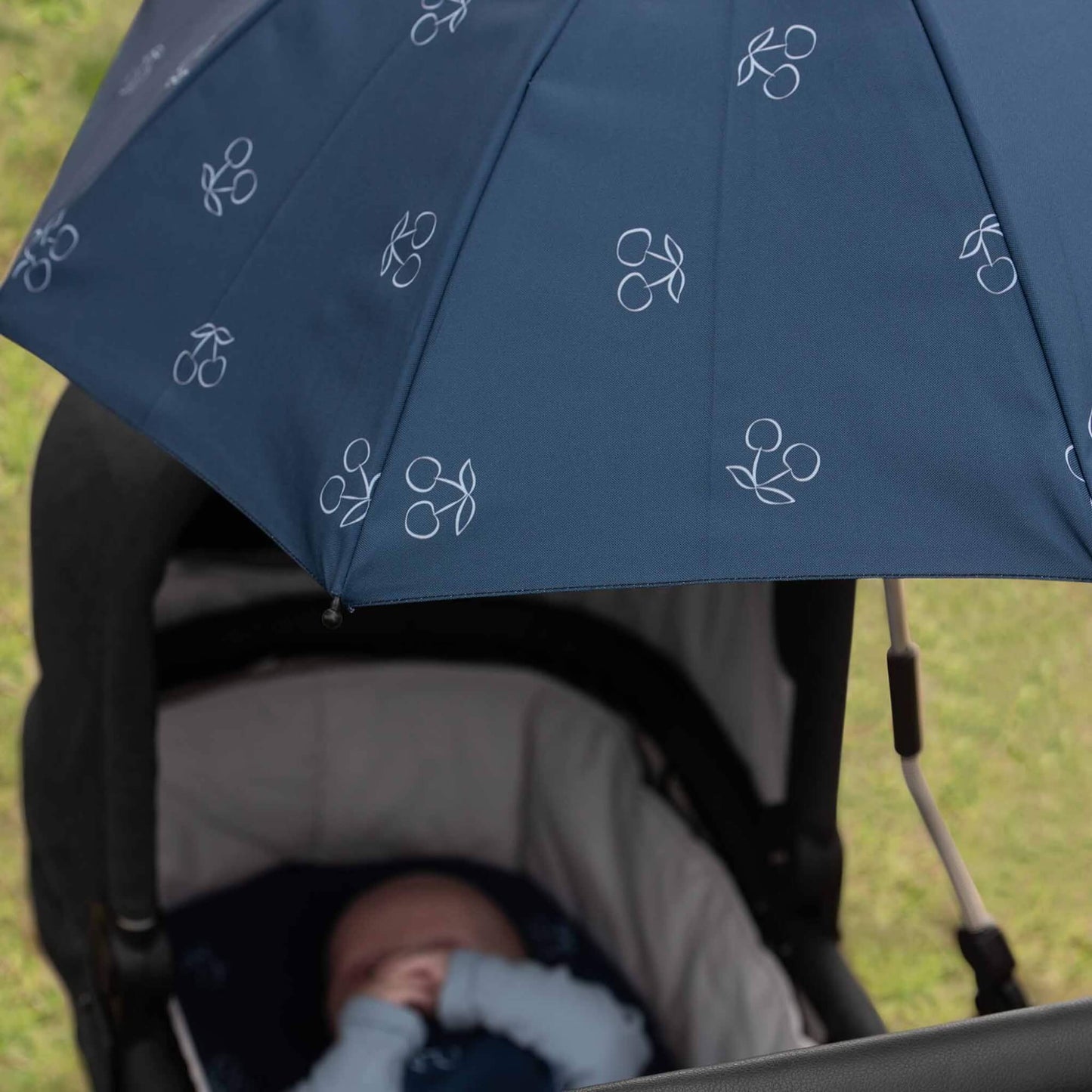 Close-up of the Dooky Blue Cherry parasol shading a baby in a pushchair, highlighting the cherry print and canopy coverage.