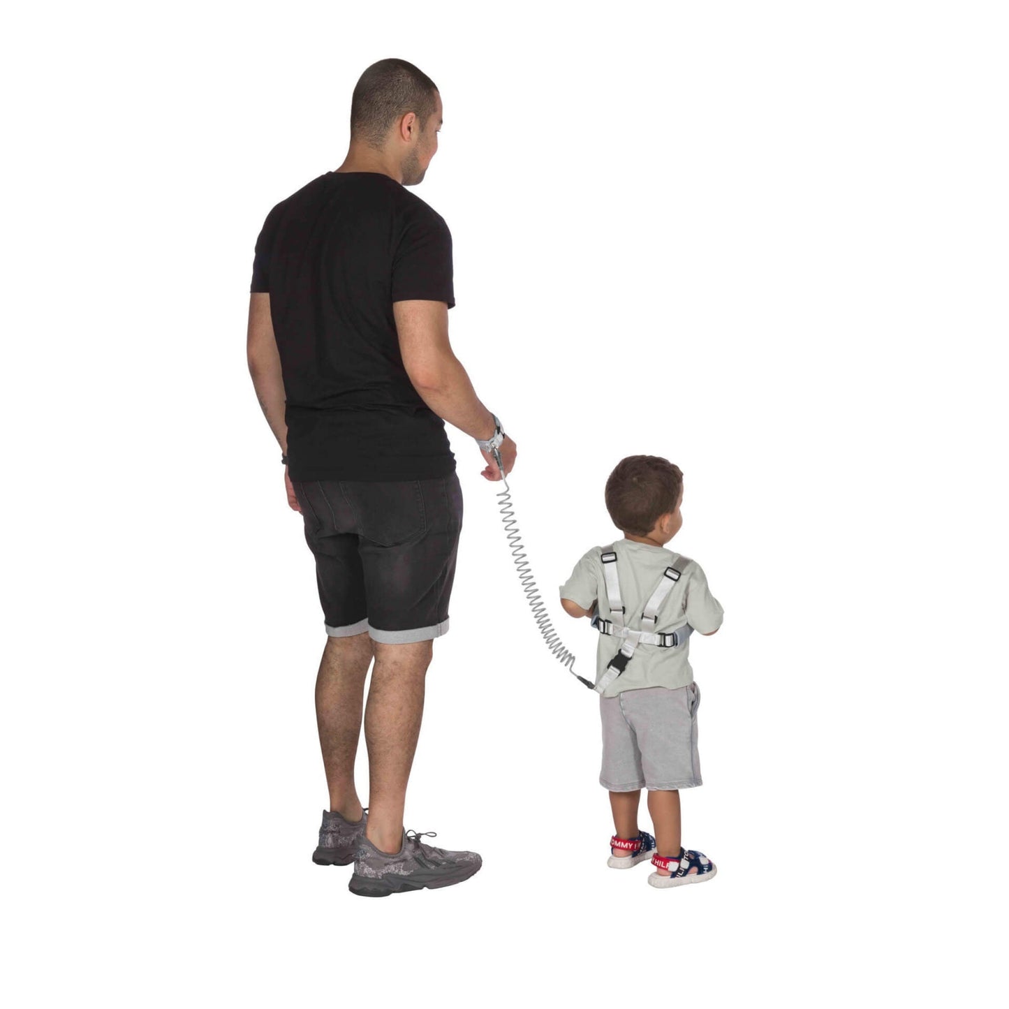 An adult and child walking away, the child wearing a safety harness connected to the adult by a coiled tether.