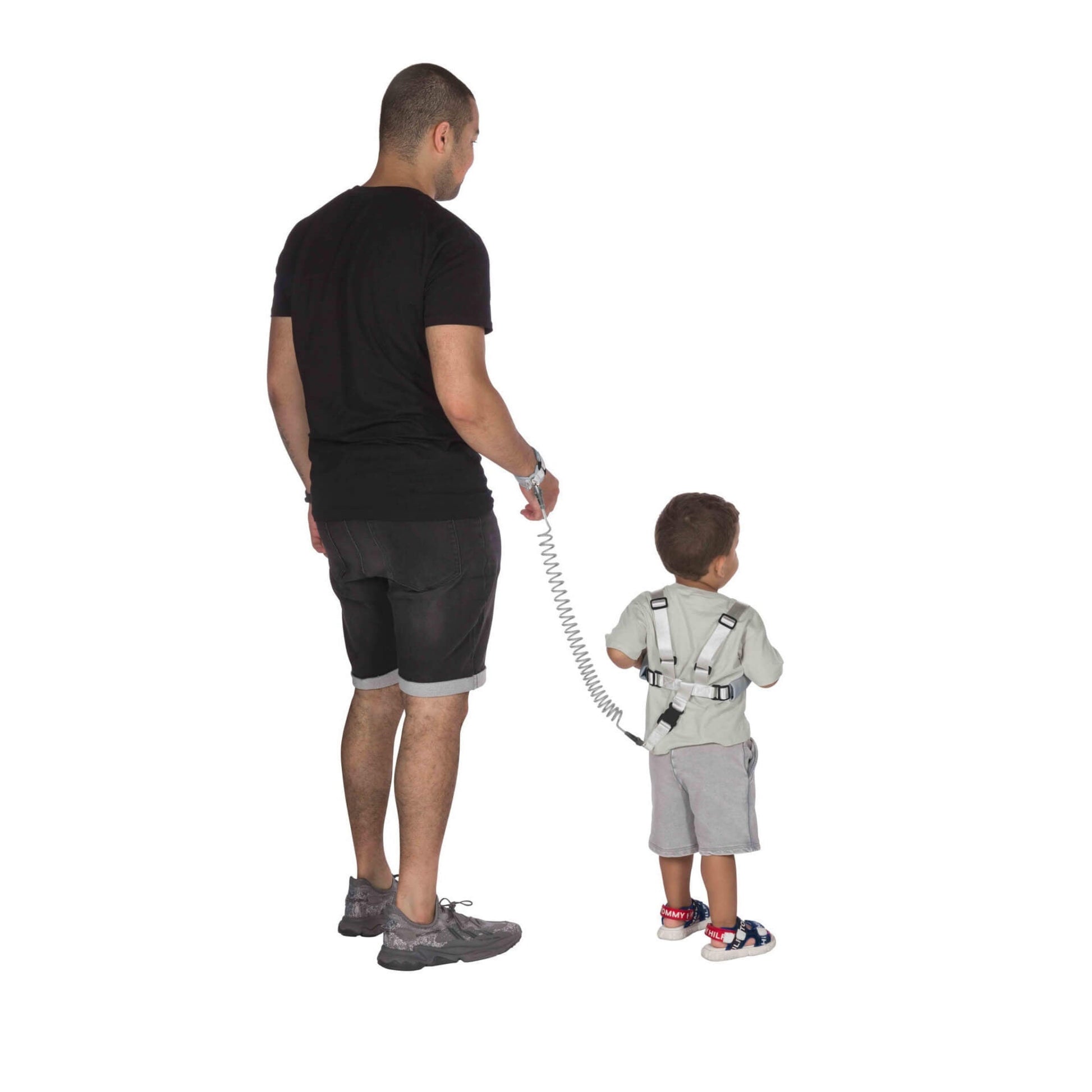 An adult and child walking away, the child wearing a safety harness connected to the adult by a coiled tether.