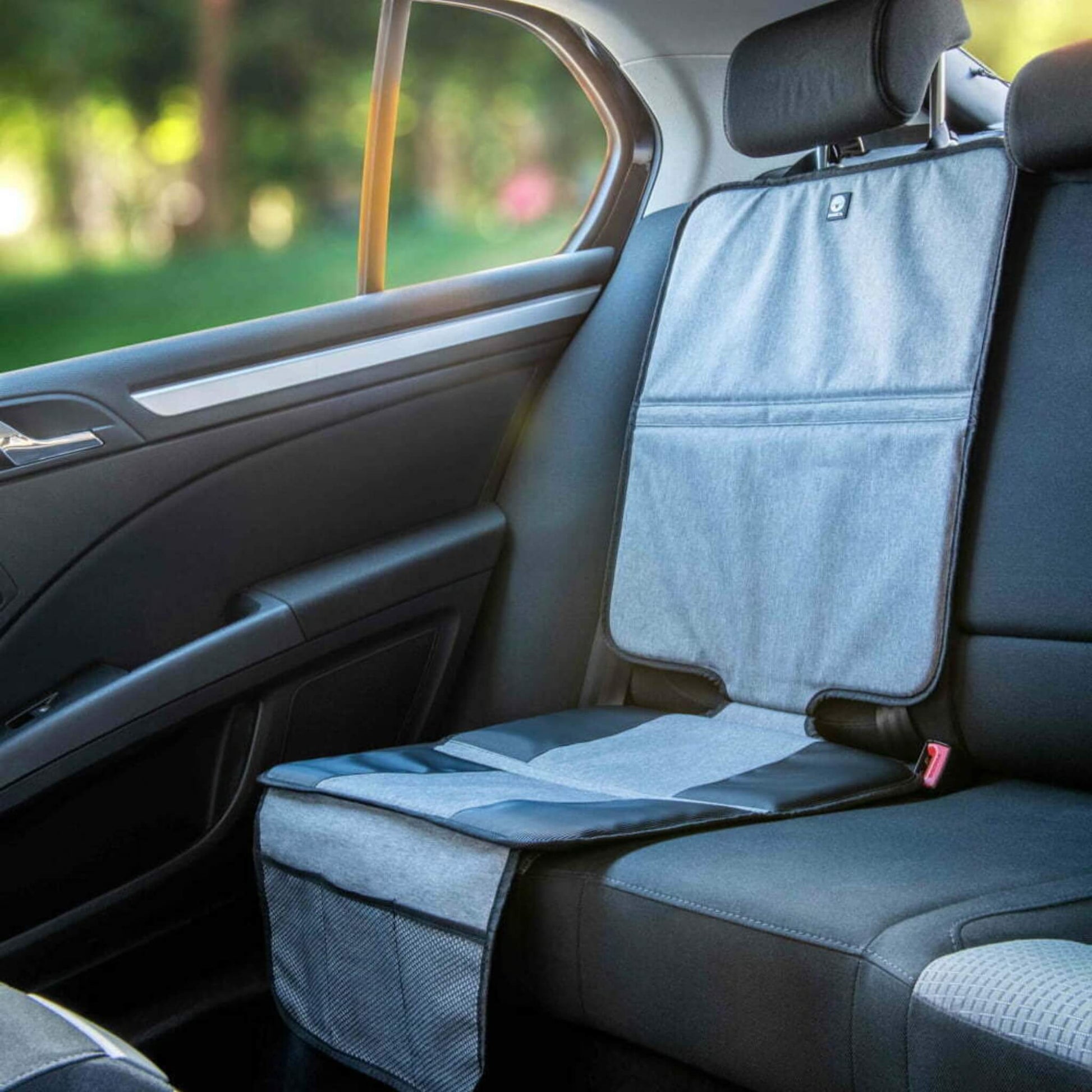 A grey and black seat protection mat secured to a rear passenger seat in a car, with mesh storage pockets hanging down the front.