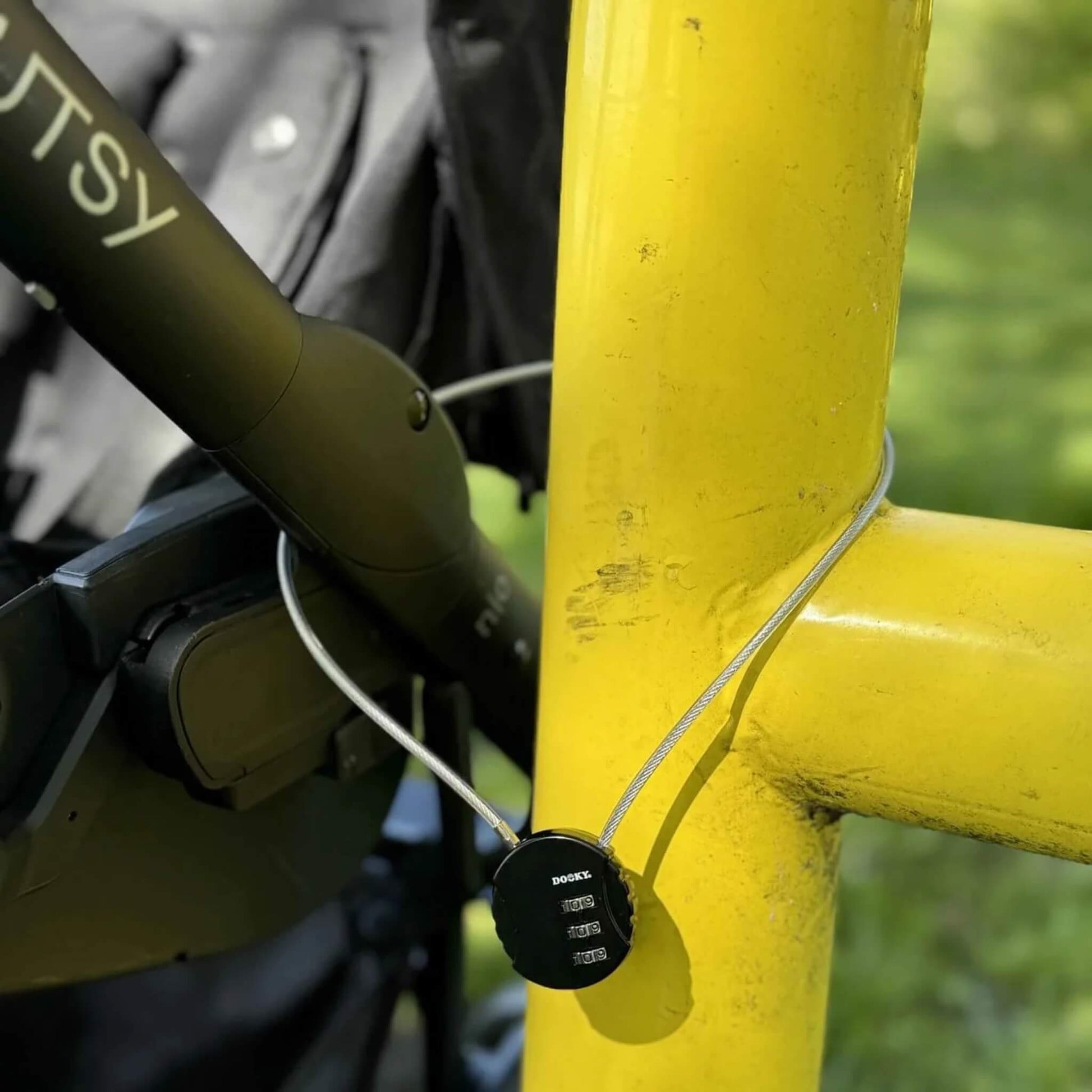 A cable lock looped through a stroller frame and attached to a yellow metal barrier outdoors.