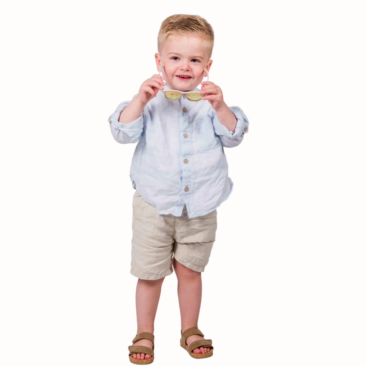 Young boy holding a pair of beige sunglasses in front of him.