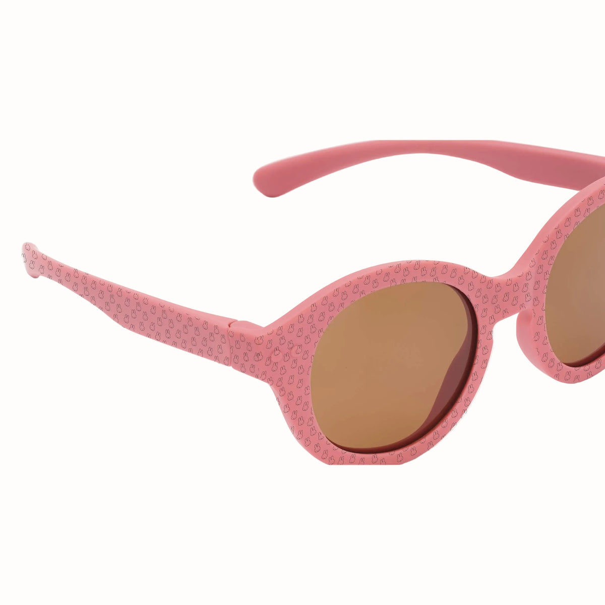Close-up of pink children’s sunglasses showing the rounded brown lenses and Miffy pattern across the frames and arms.