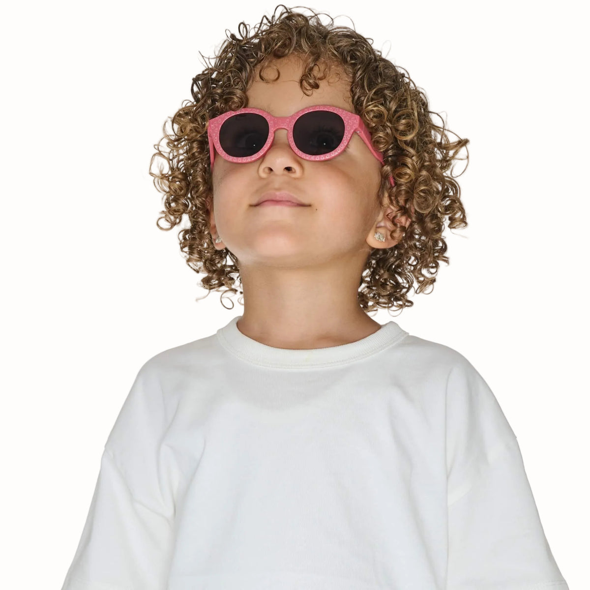 Child wearing pink patterned sunglasses with rounded dark lenses and a white T-shirt.
