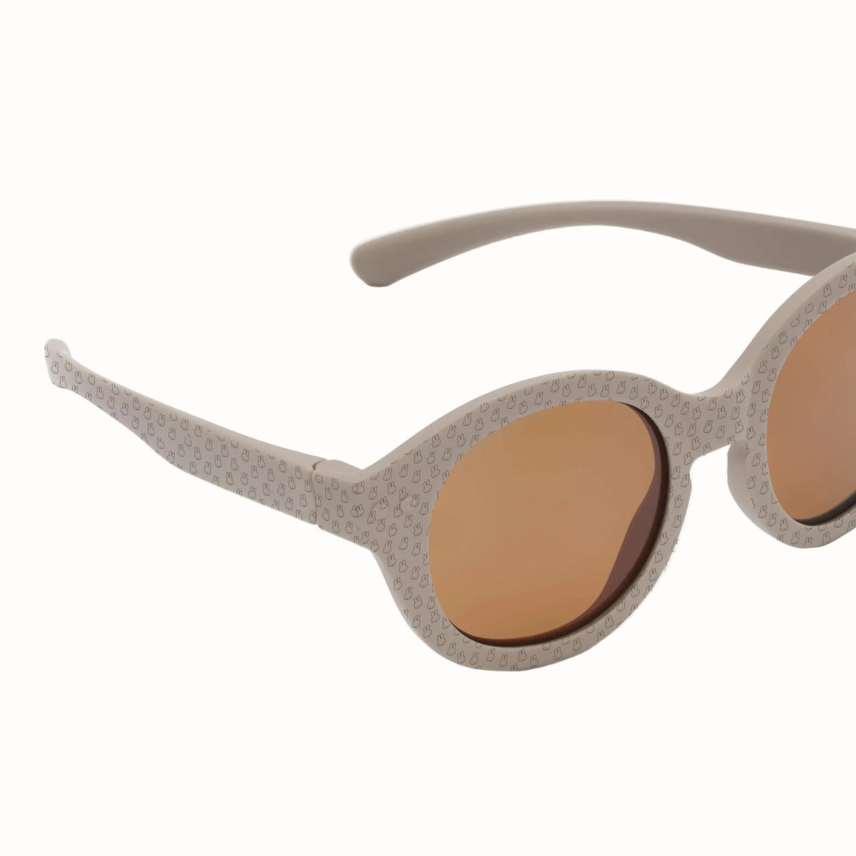 Close-up of taupe children's sunglasses showing rounded brown lenses and tiny bunny pattern across the frames and arms.
