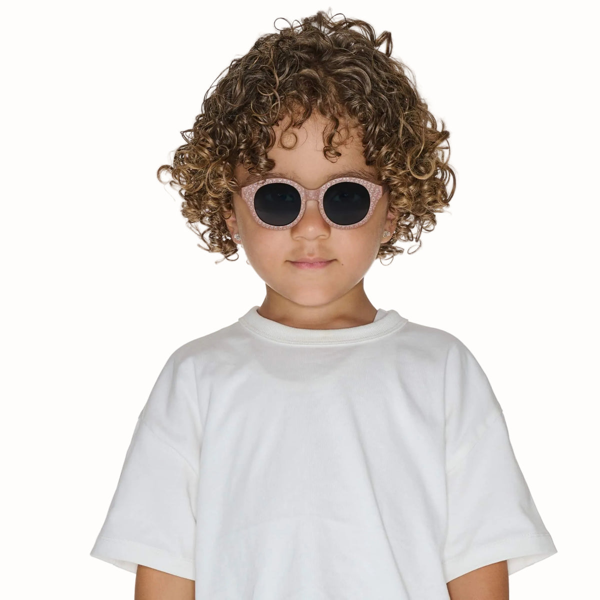 Child wearing taupe patterned sunglasses with rounded dark lenses and a white T-shirt.