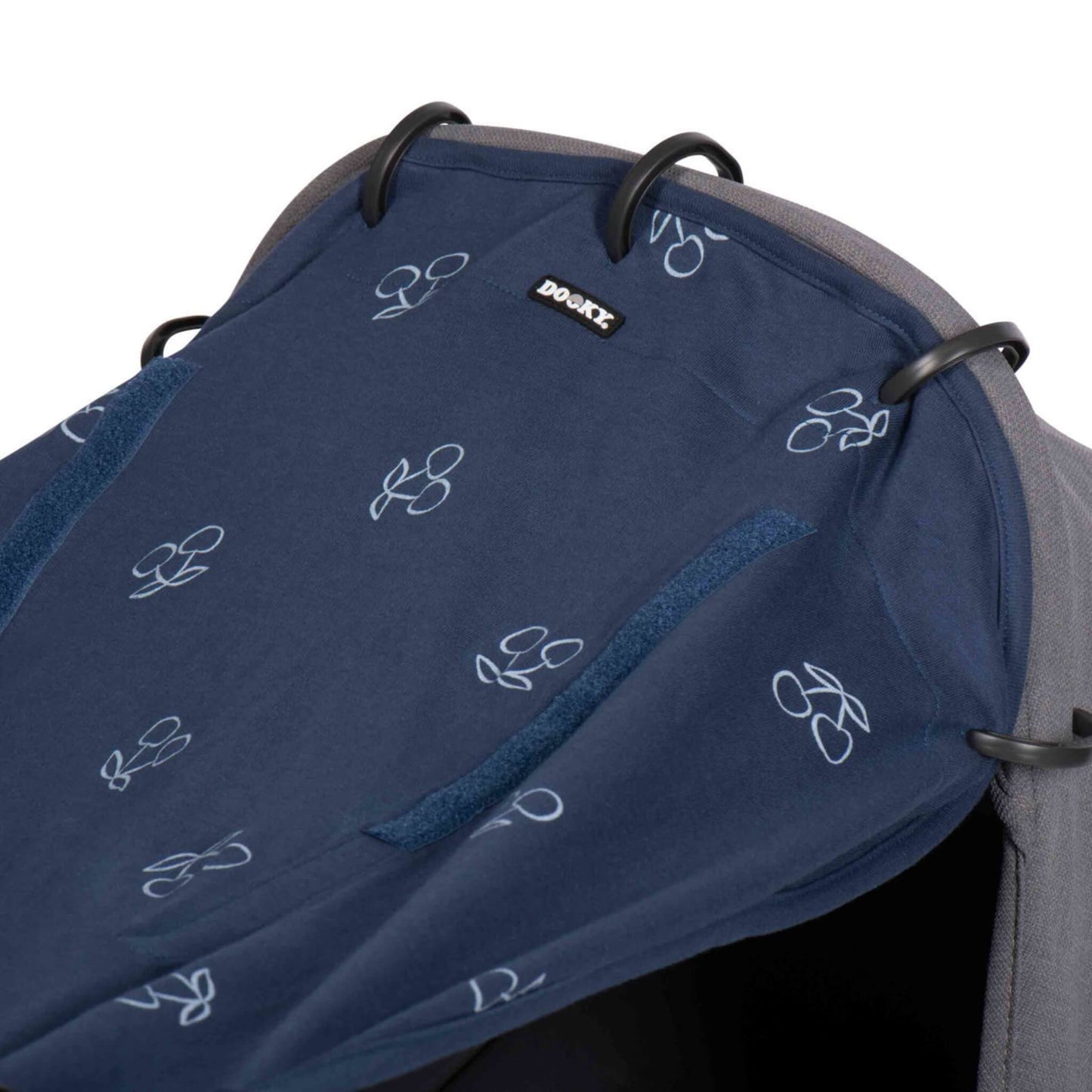 Close-up of the upper edge of the sunshade secured to a pram hood using three plastic rings. Two Velcro strips are visible beside the Dooky logo.