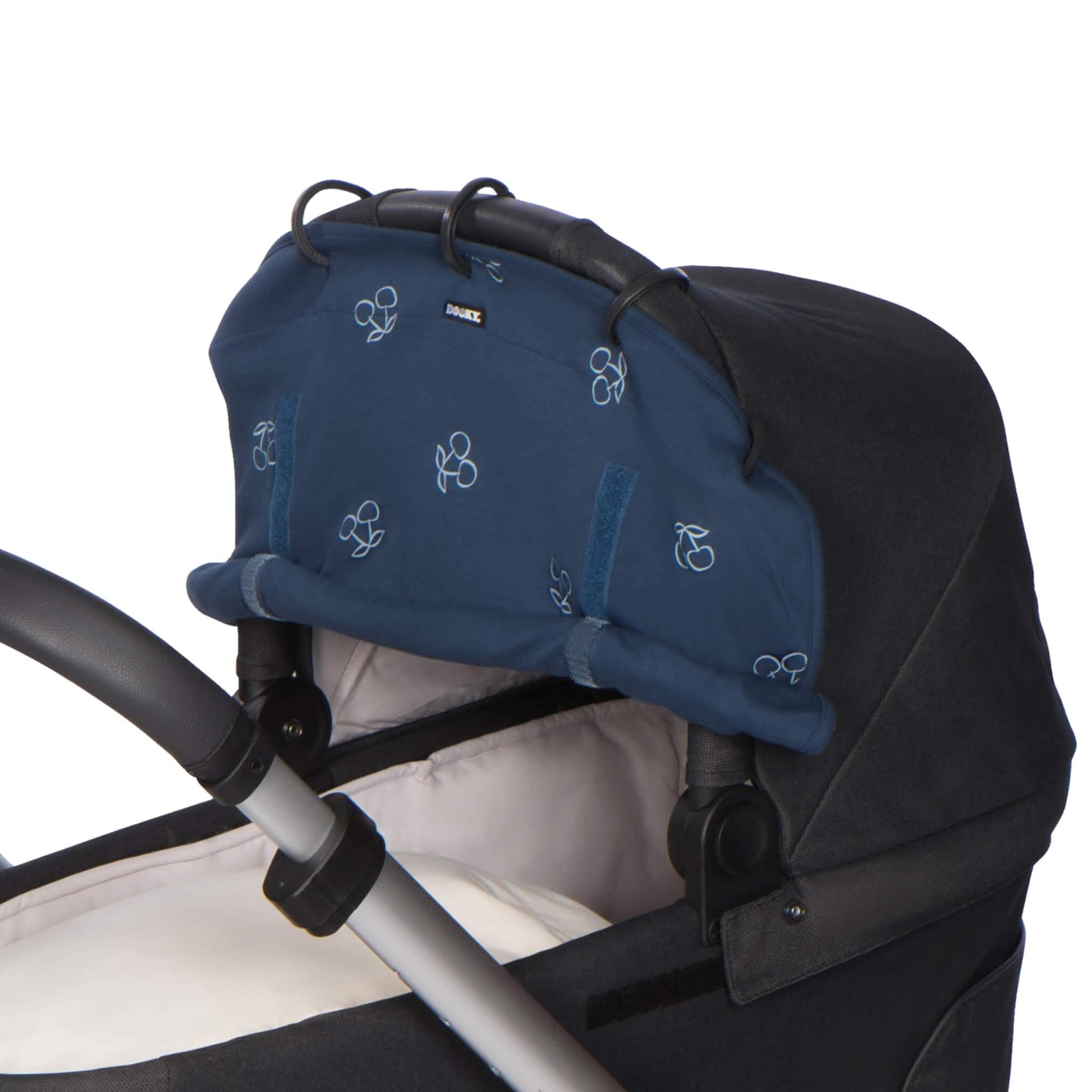 Side view of a navy blue sunshade with cherry print attached to a carrycot hood, partially rolled up and secured with Velcro. The pram handle is visible beneath.