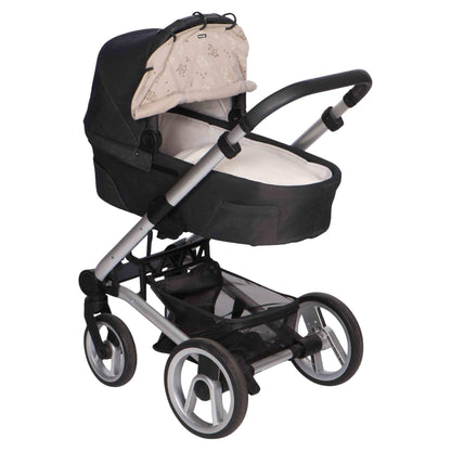 A beige printed sunshade secured to the canopy of a black carrycot on a silver-framed pram.