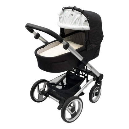 A leaf-patterned fabric sunshade clipped to a black pram carrycot canopy, shown from a side angle on a silver pushchair frame.