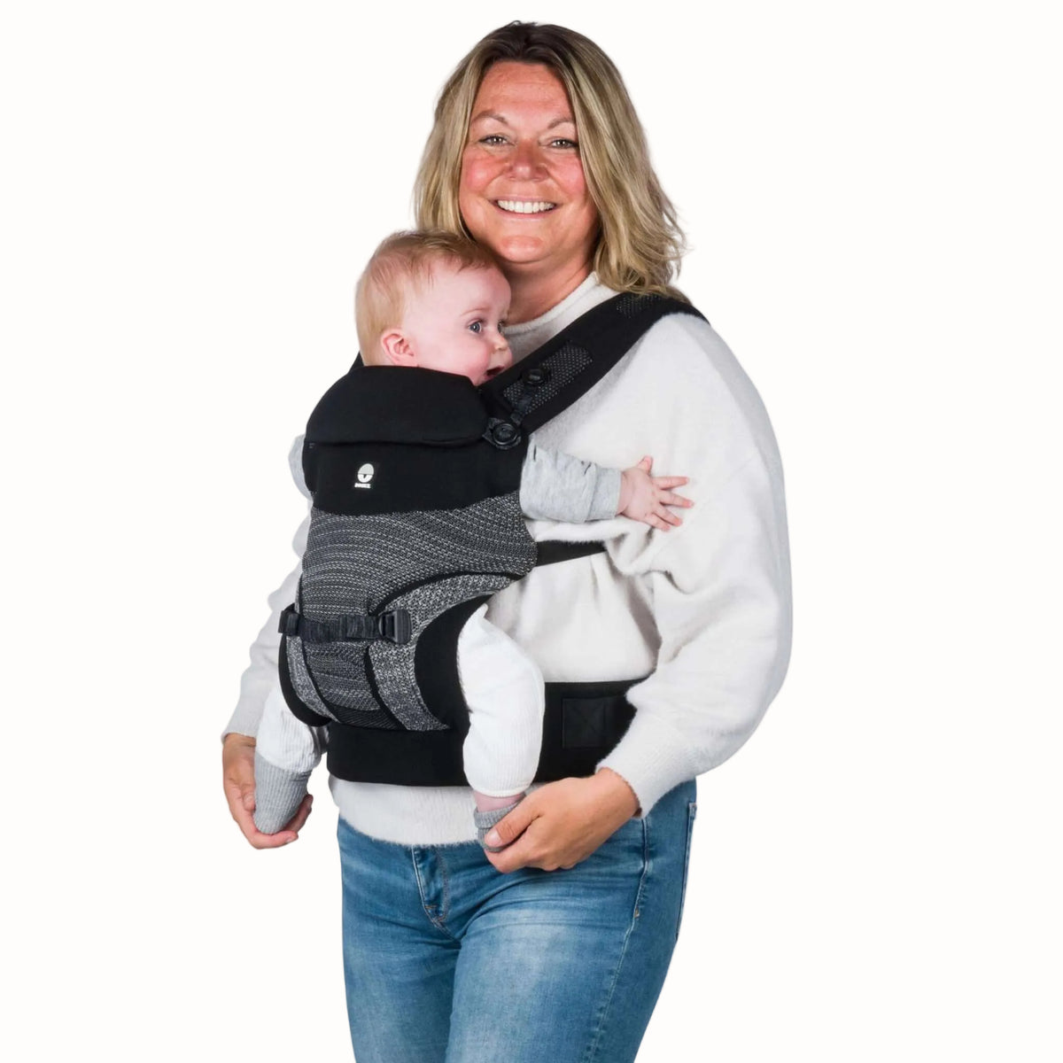 A parent wearing a baby facing inward in a black baby carrier, with the padded waist belt and shoulder straps visible.