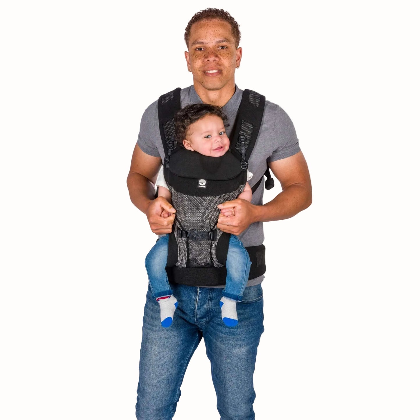 A father carrying a baby facing inward in a black baby carrier, showing the supported seated position.