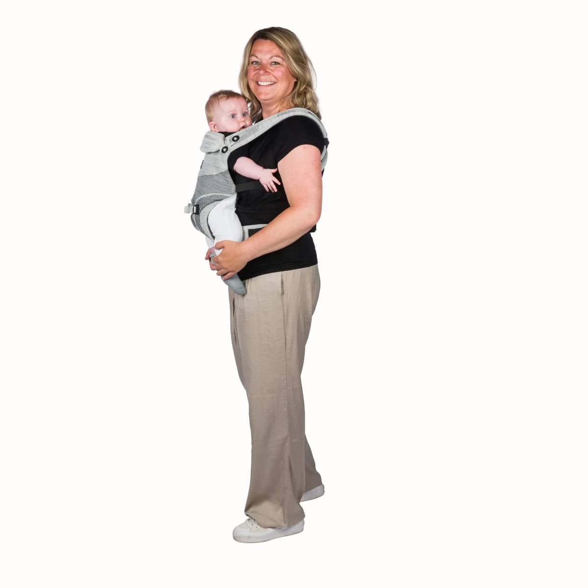 Side view of a parent carrying a baby facing inward in a grey baby carrier with a wide padded waist belt.