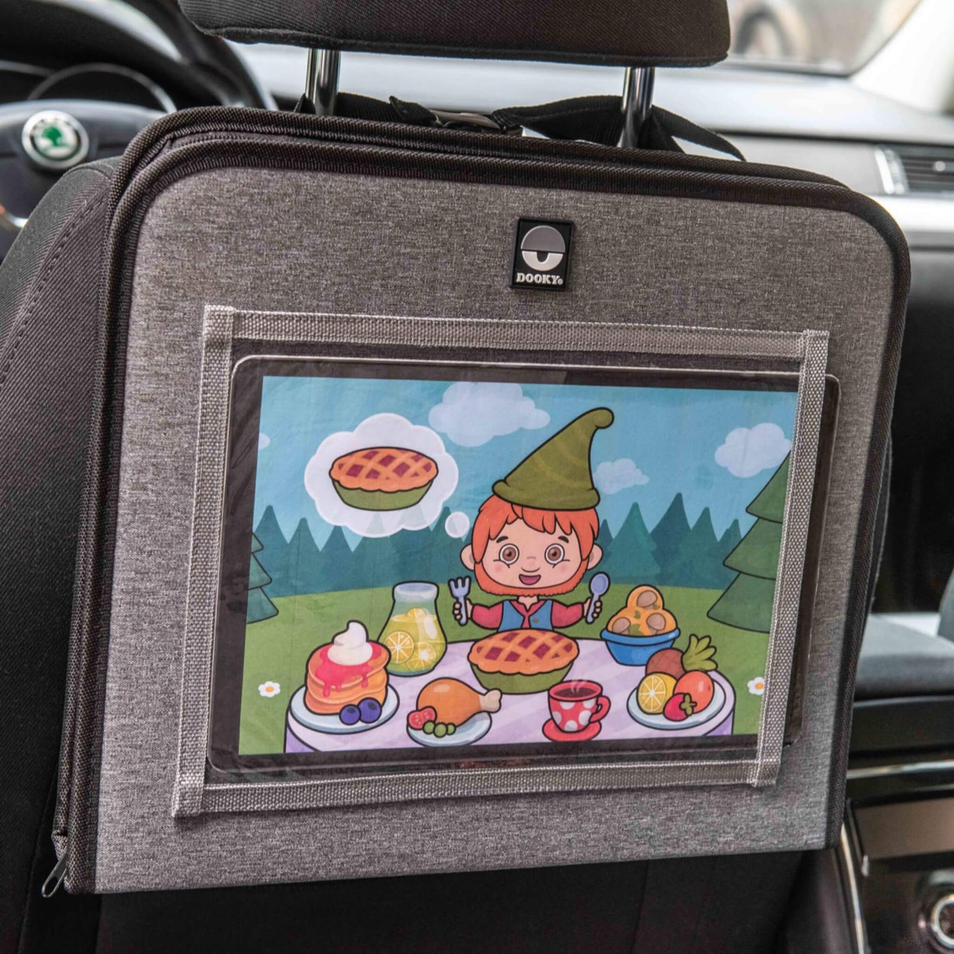 A car seat travel tray clipped to the back of a car seat with a tablet playing a cartoon featuring a child-friendly picnic scene.