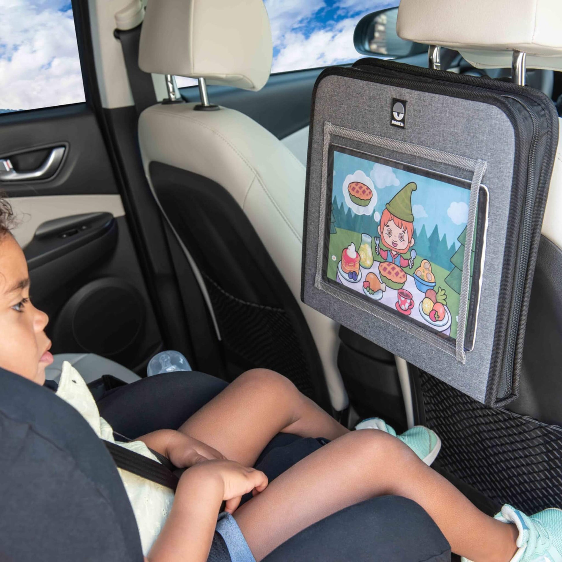 A child in a car seat watching a cartoon on a tablet held securely in a grey back seat organiser.