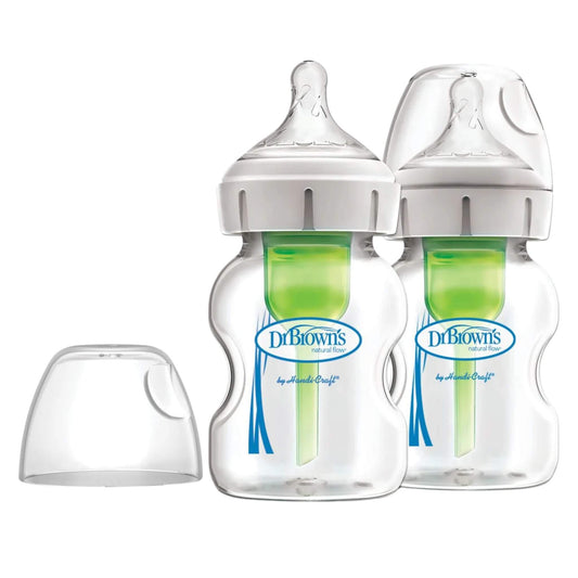 Two Dr Brown’s glass baby feeding bottles with green internal vent systems and clear protective caps, with one spare cap beside them on a white background.
