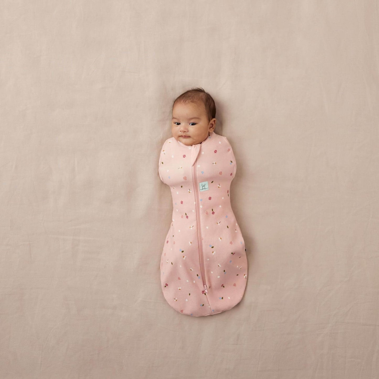 Baby snuggled in a Cocoon Swaddle Bag in a soft pink daisies print, offering a cosy, secure fit for peaceful sleep.