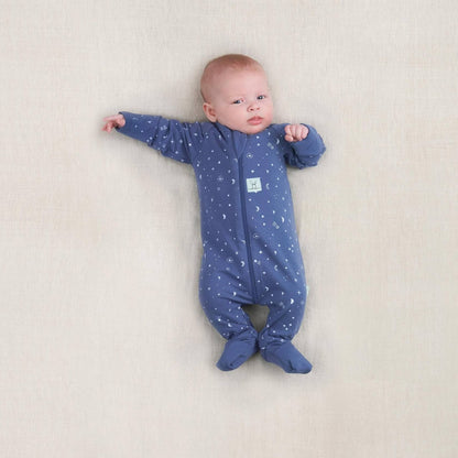 Newborn baby wearing a blue cotton babygrow with moon and star print, lying on a neutral surface with arms outstretched.