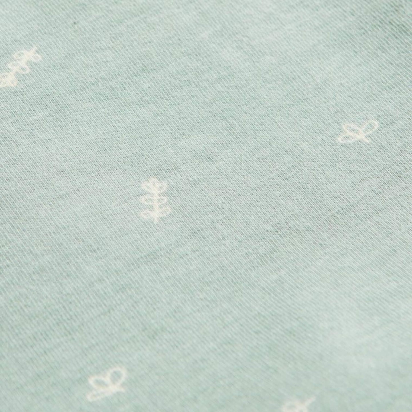 Close-up of Sage green jersey fabric with scattered white leaf and sprig motifs from the babygrow design.