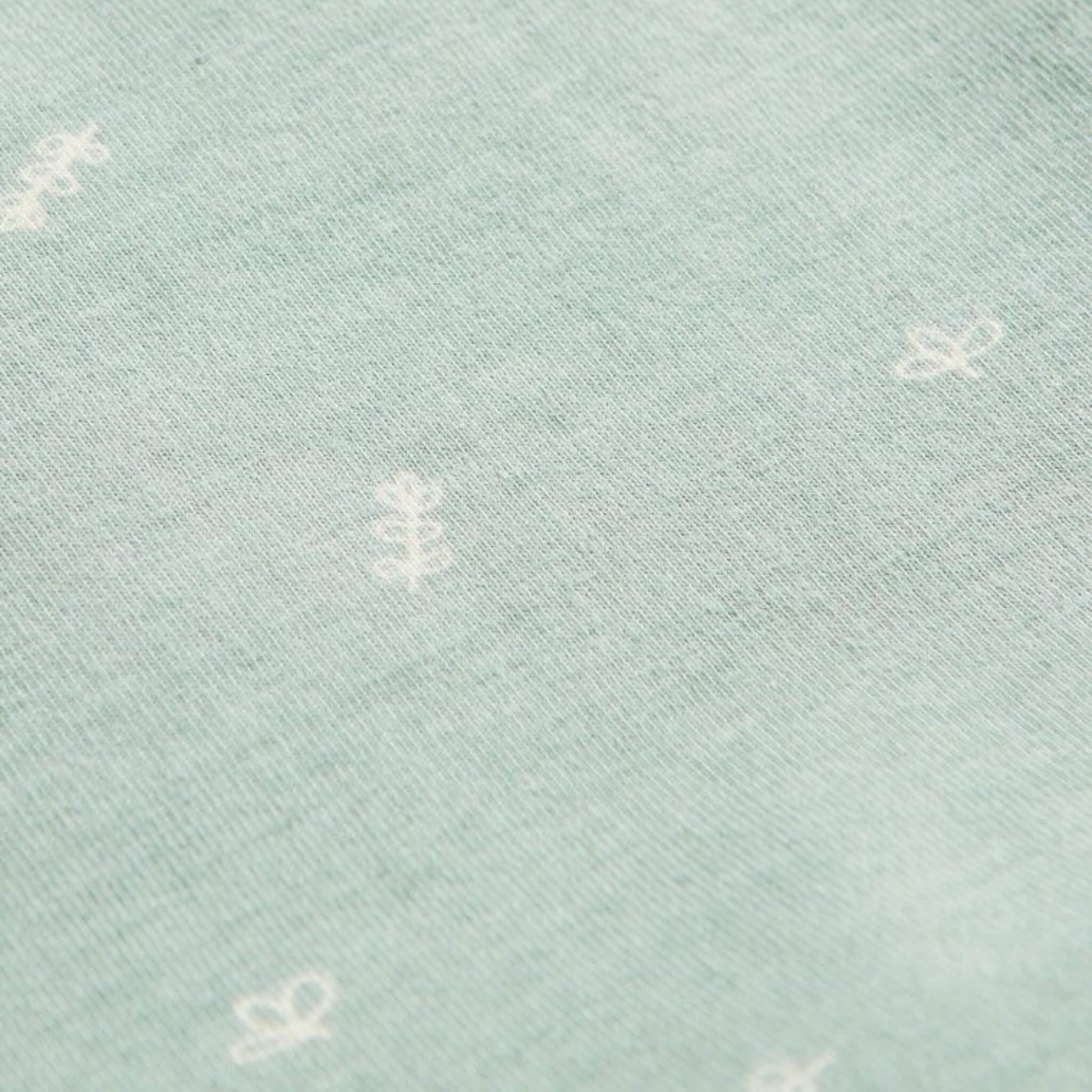 Close-up of Sage green jersey fabric with scattered white leaf and sprig motifs from the babygrow design.