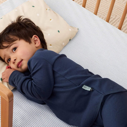 Toddler lying on their side in a cot, head on a beige pillow patterned with white daisies and scattered green leaves.